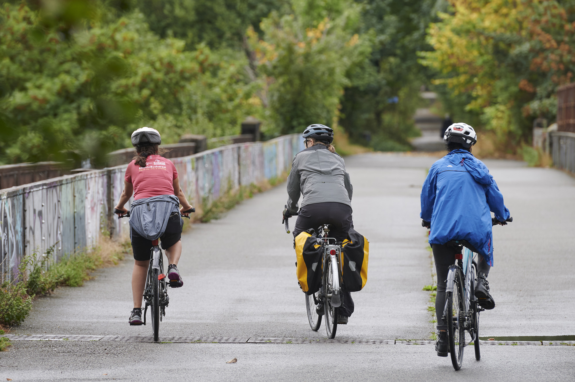 3 cyclists, wearing helmets, cycling over bridge in Avenham Park