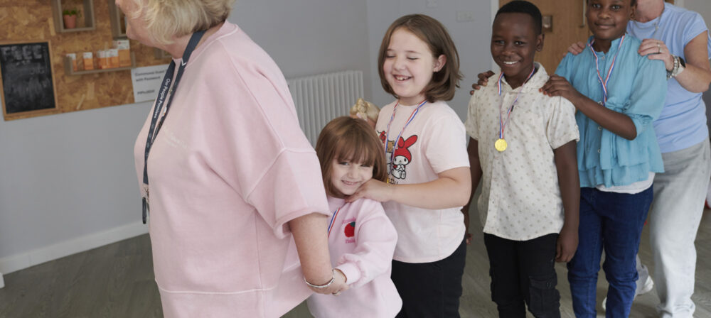 Two happy adult females leading a conga line of four happy children aged four - six