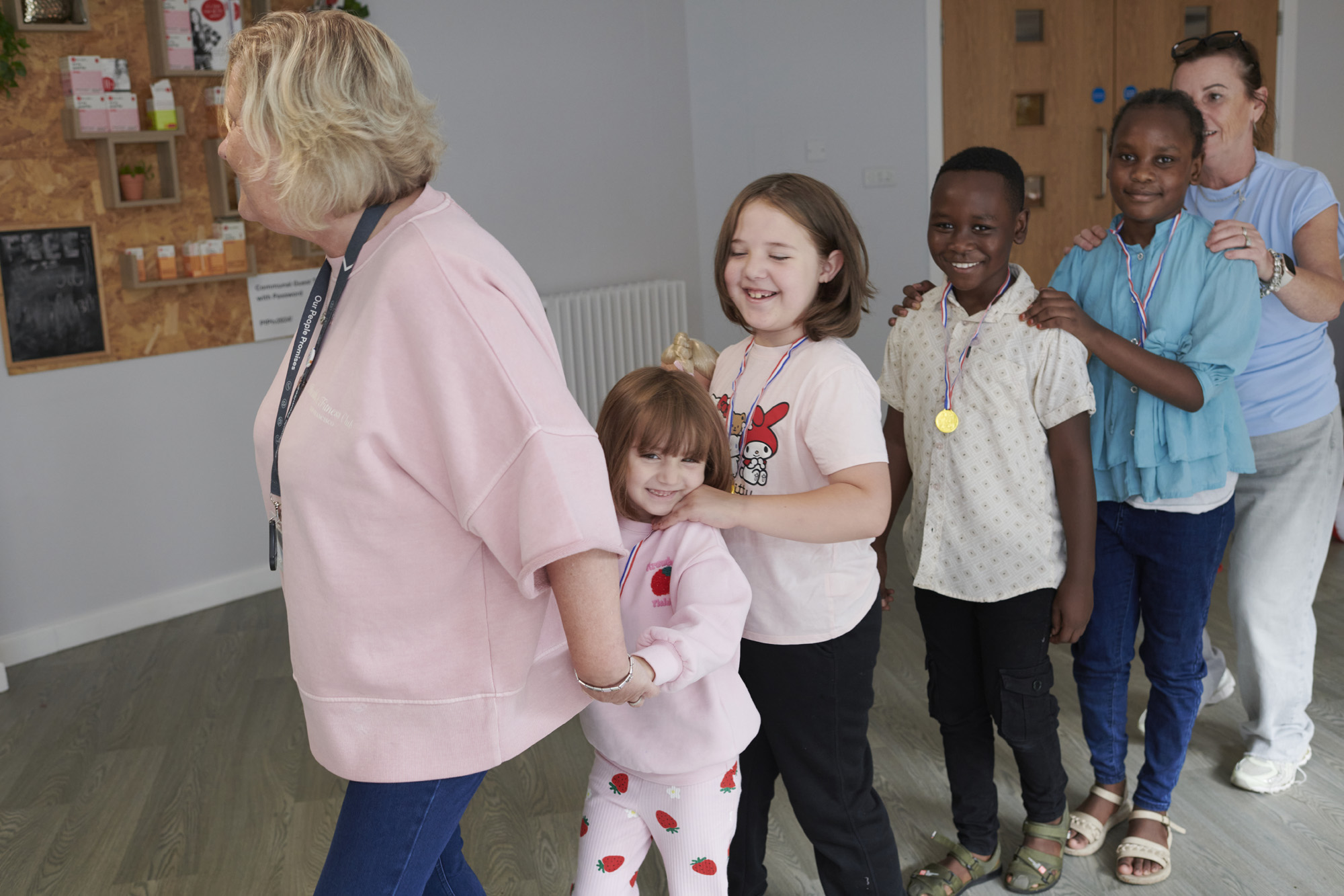 Two happy adult females leading a conga line of four happy children aged four - six