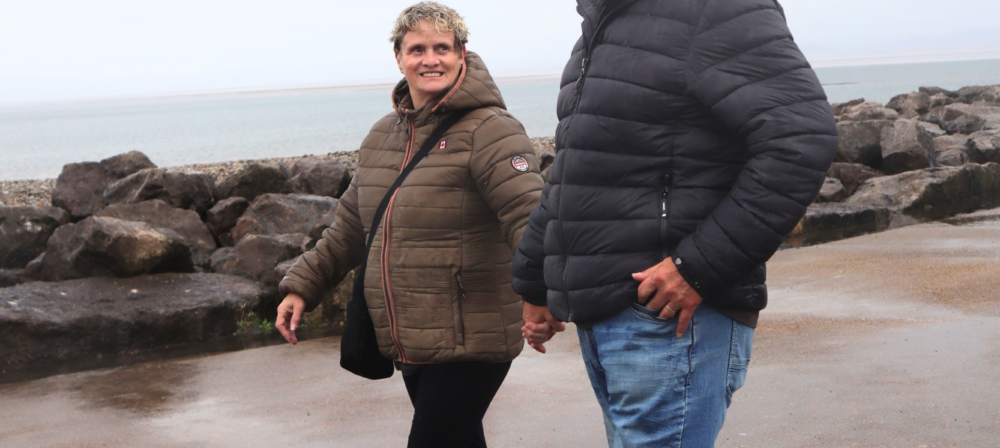 Couple walking along the shoreline holding hands and looking towards eachother