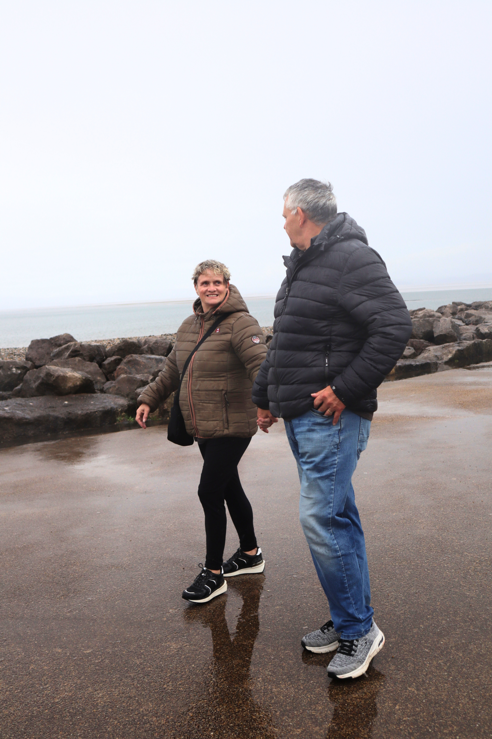 Couple walking along the shoreline holding hands and looking towards eachother