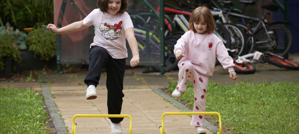 Two happy young girls playing with mini-hurdles outside