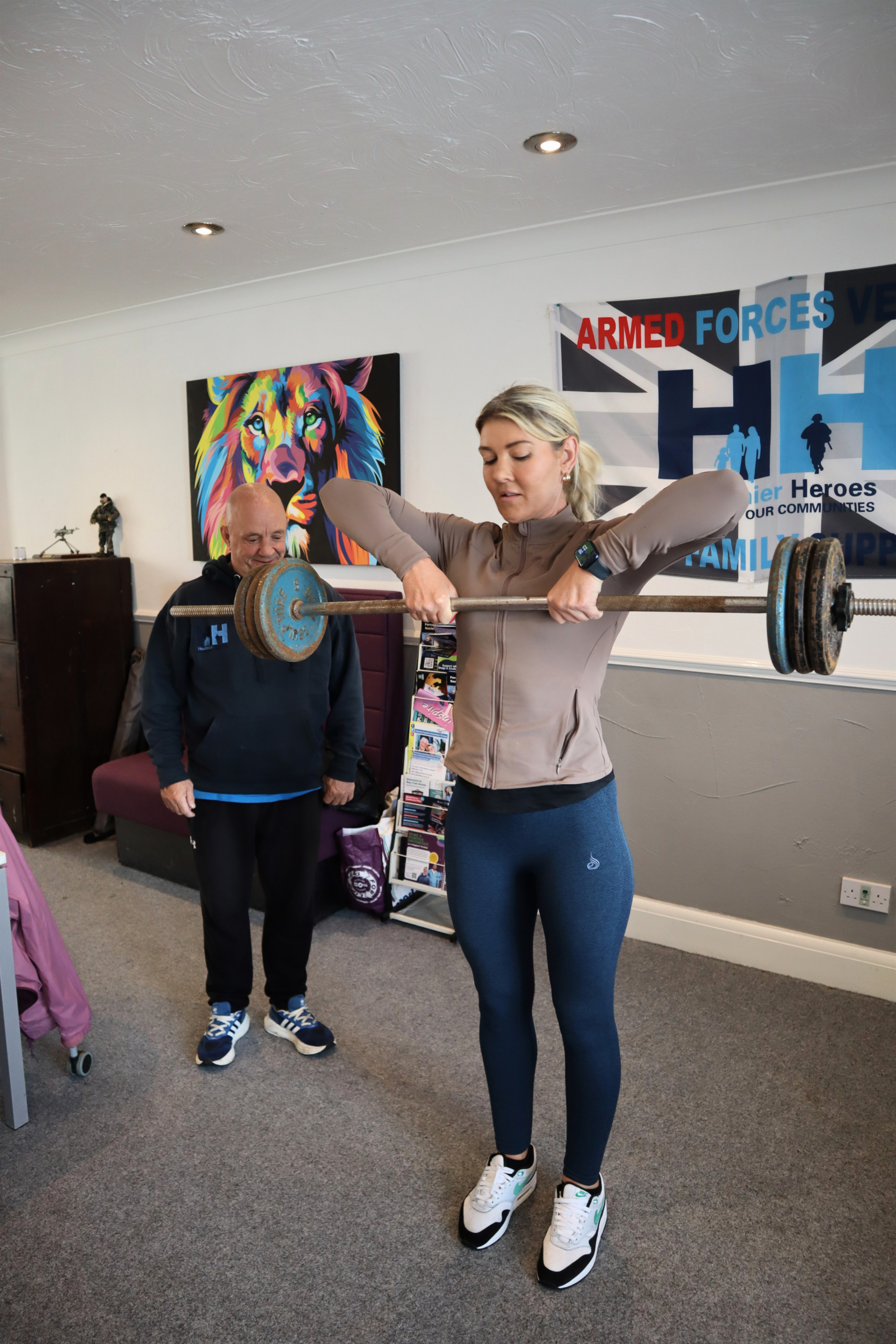 Woman lifting a barbell with a coach nearby