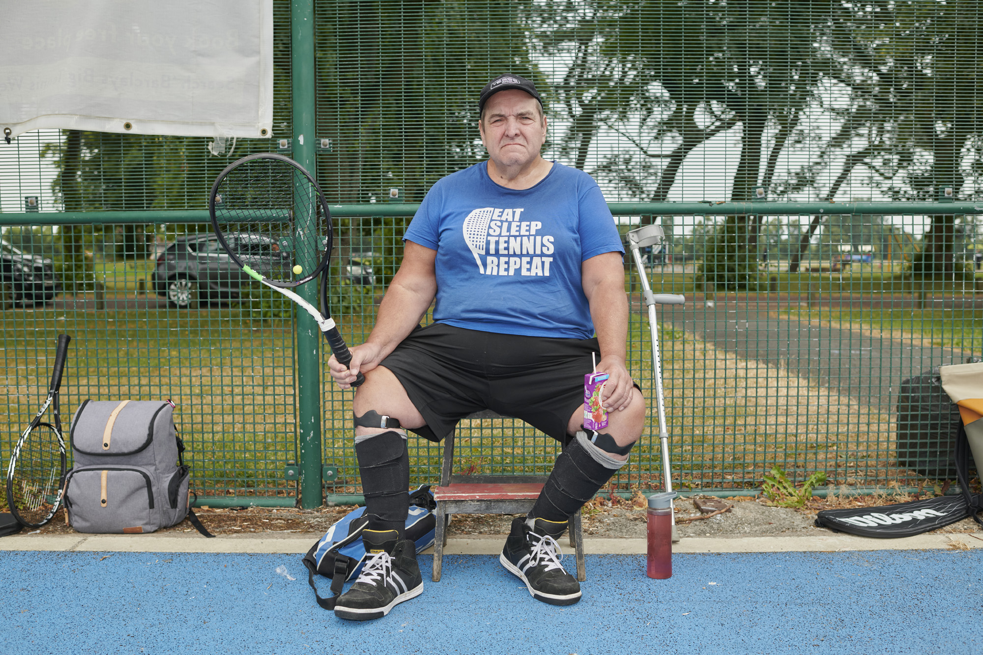 Male sitting next to net on tennis court, holding racket