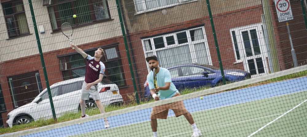 Two males playing tennis on tennis court at Moor Park