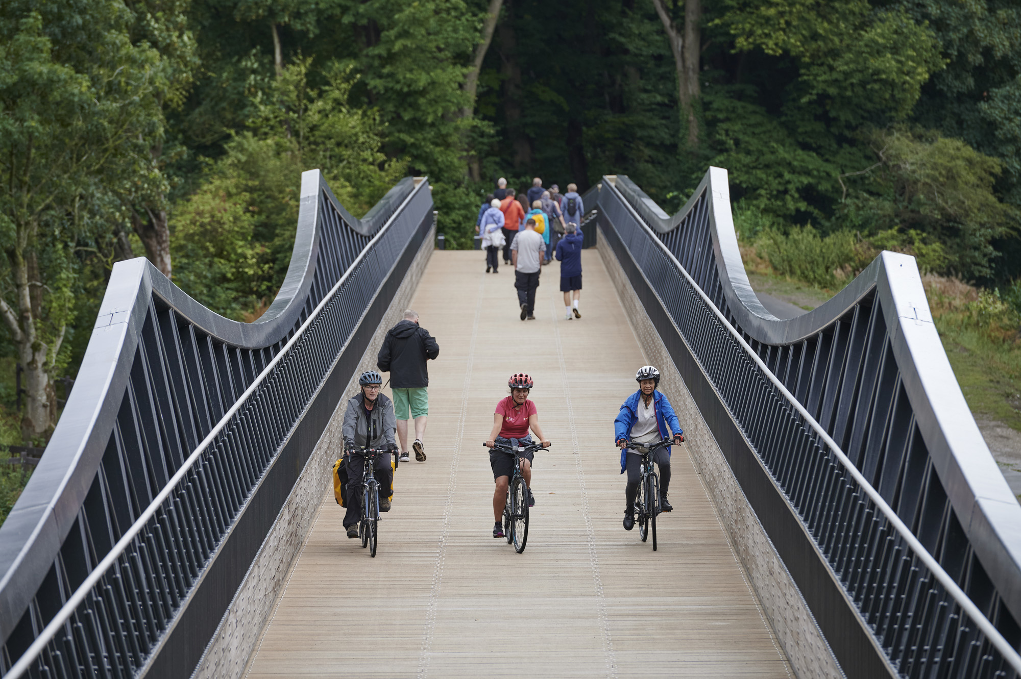 Three cyclists, wearing helmets, cycling over Tram Bridge, at a distance