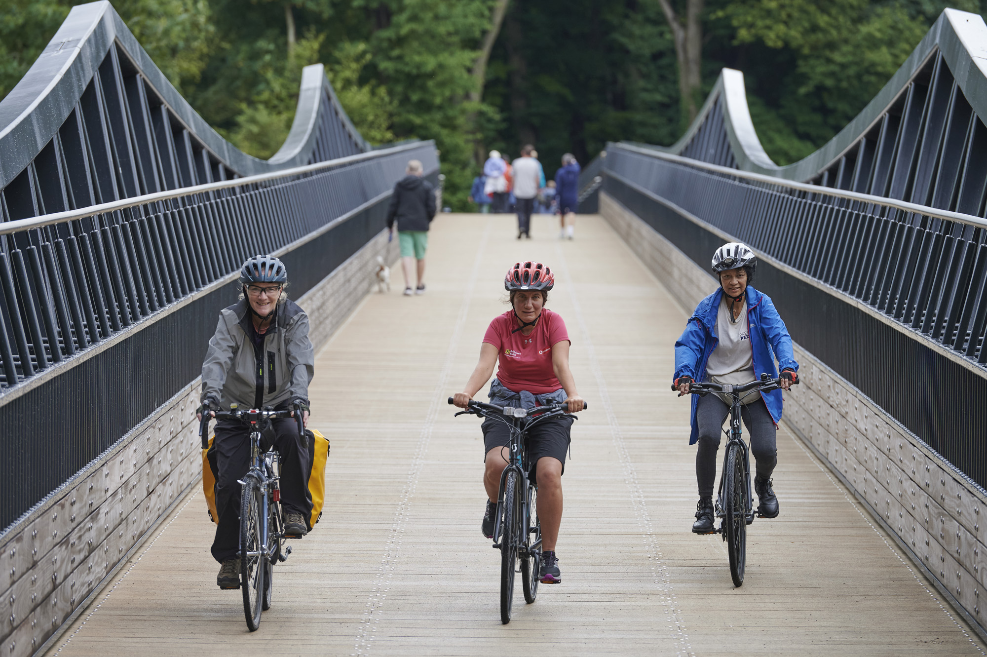 Three female cyclists, wearing helmets, cycling across Tram Bridge towards the camera