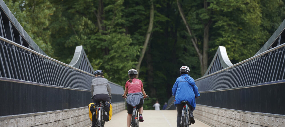 Three cyclists riding away from camera across Tram Bridge