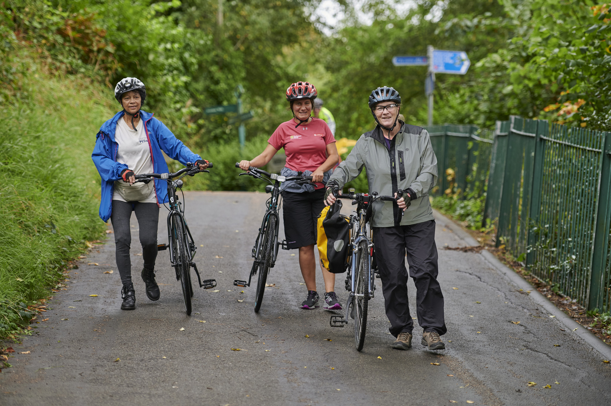 Three female cyclists, wearing helmets, standing with their bikes