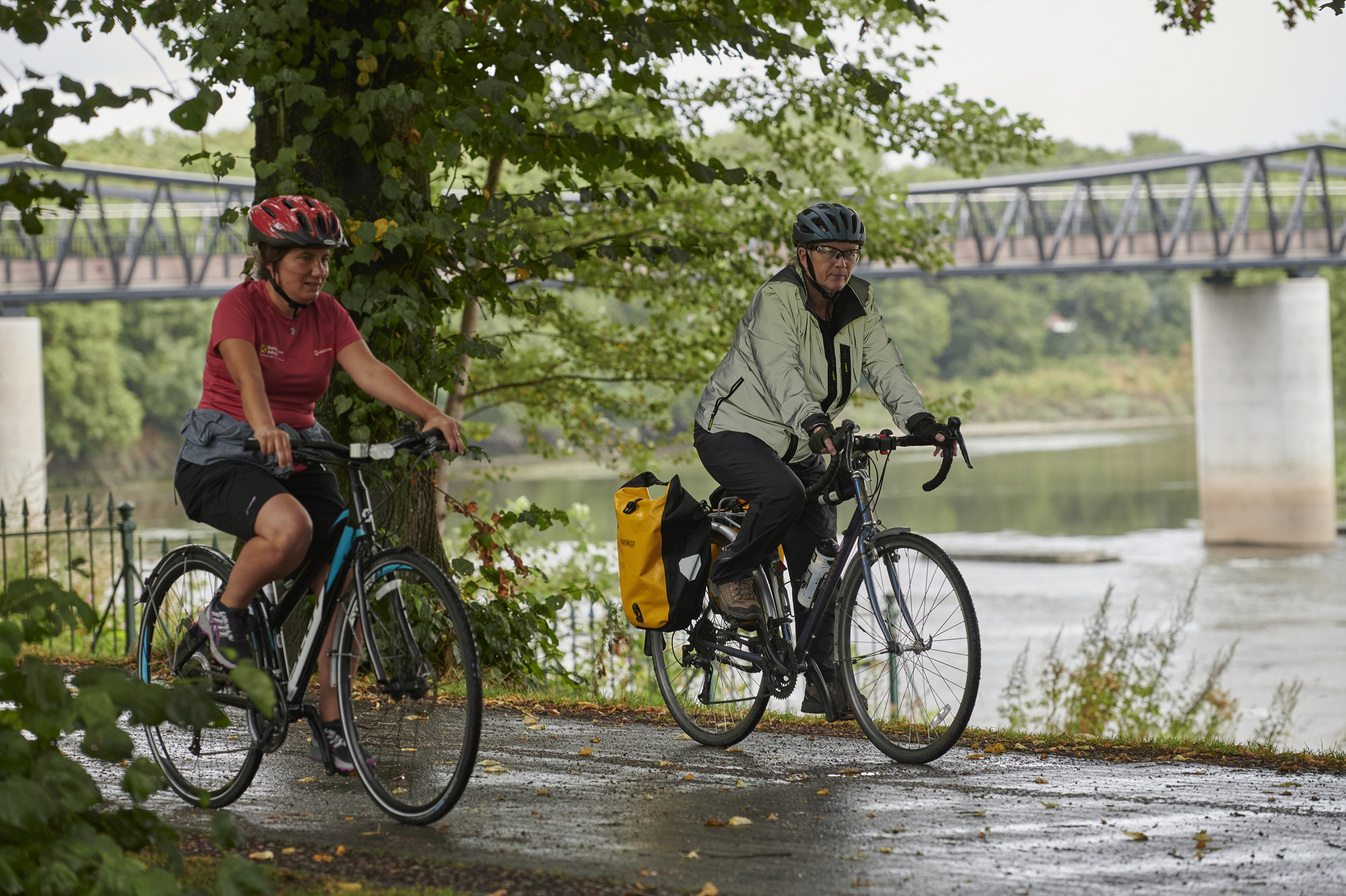 Two female cyclists, wearing helmets, cycling down path