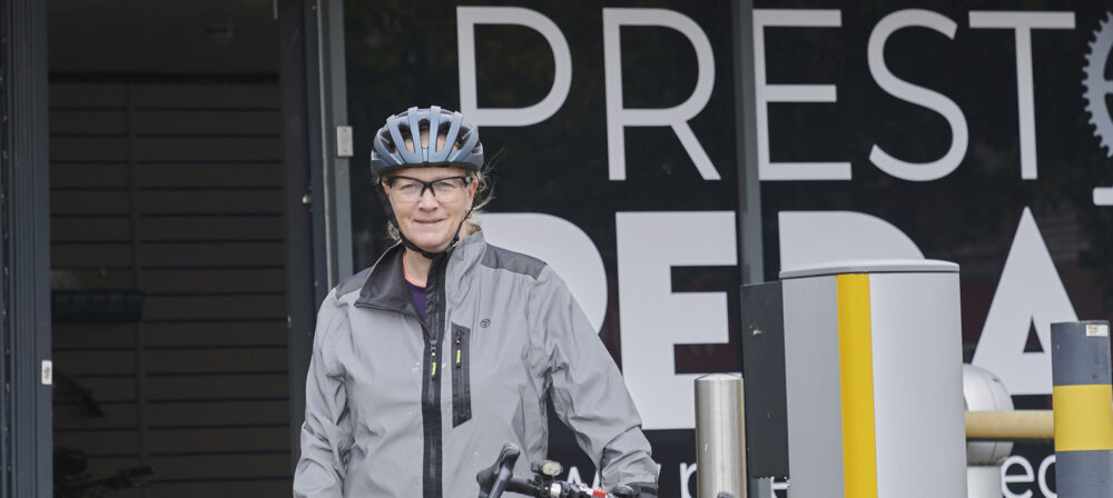 Cyclist, wearing helmet, standing with bike outside Preston Pedals