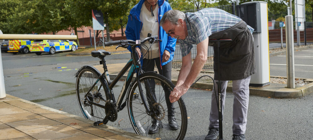 Male checking front wheel of bike whilst male cyclist, wearing helmet, holds handlebars of bike