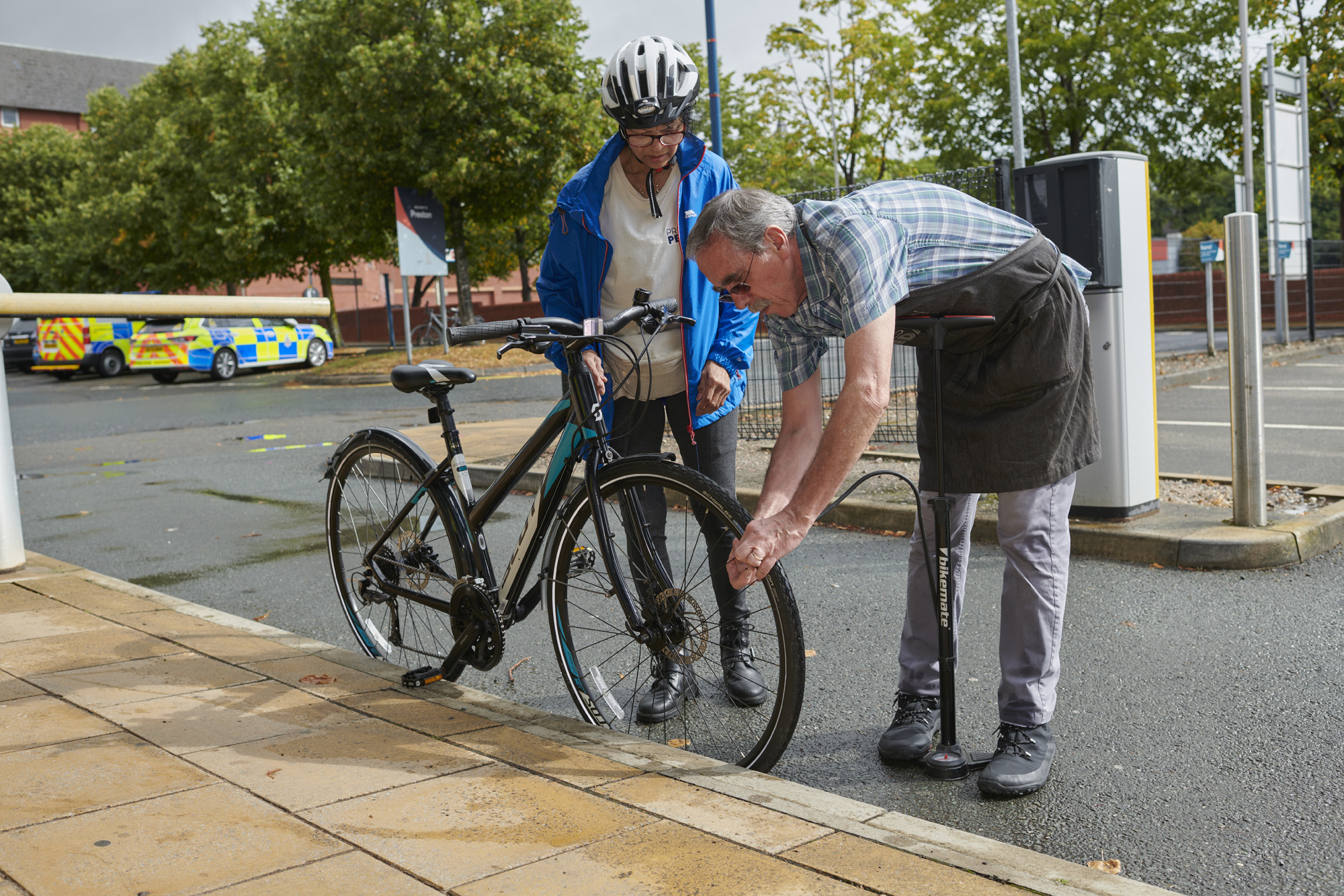 Male checking front wheel of bike whilst male cyclist, wearing helmet, holds handlebars of bike