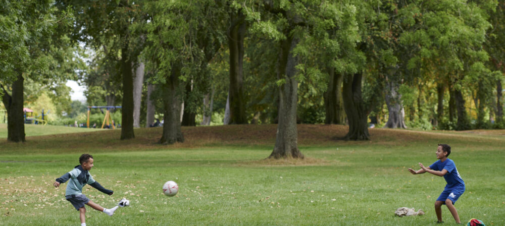 Two young brothers playing football together in Moor Park