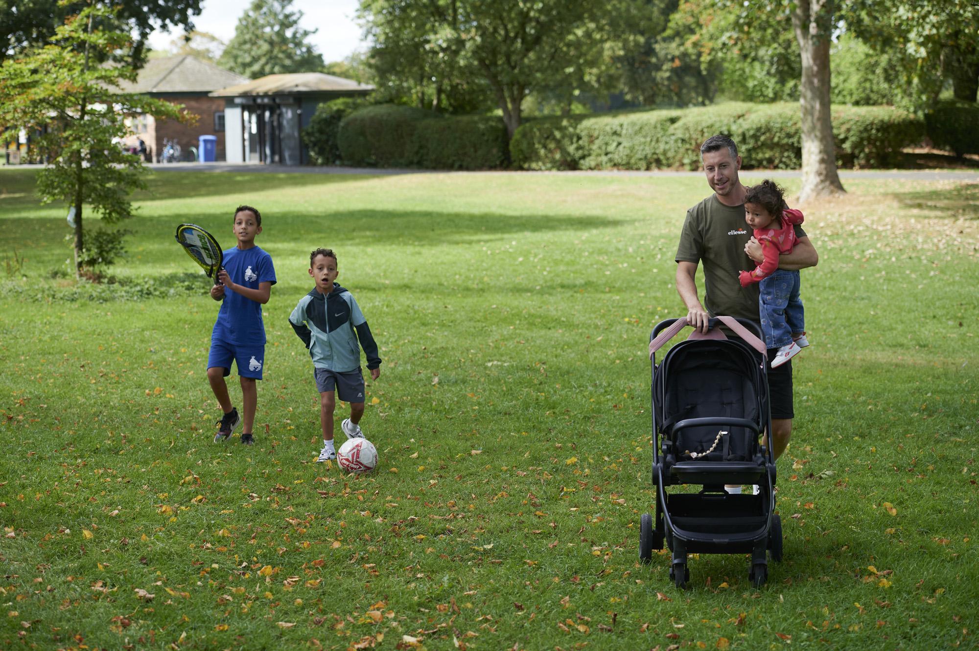 Father holding baby daughter whilst pushing the pram, two brothers walking beside the pram