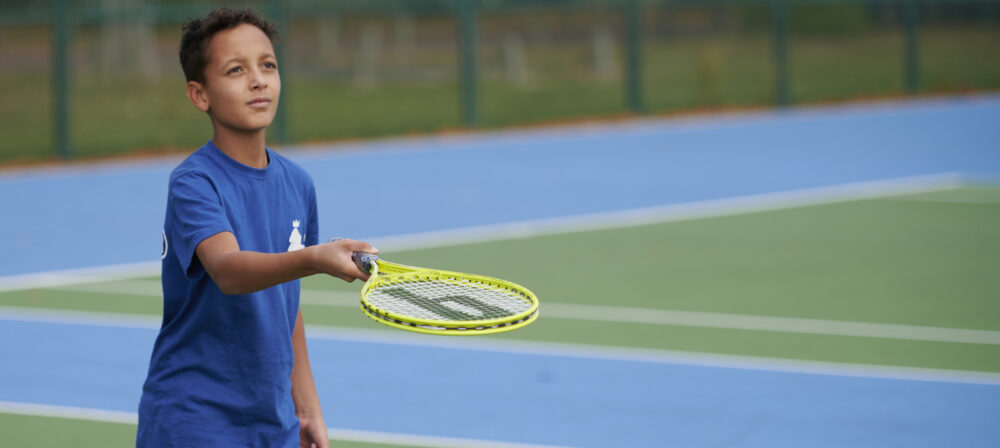Young boy with tennis racket and tennis ball on tennis court in Moor Park