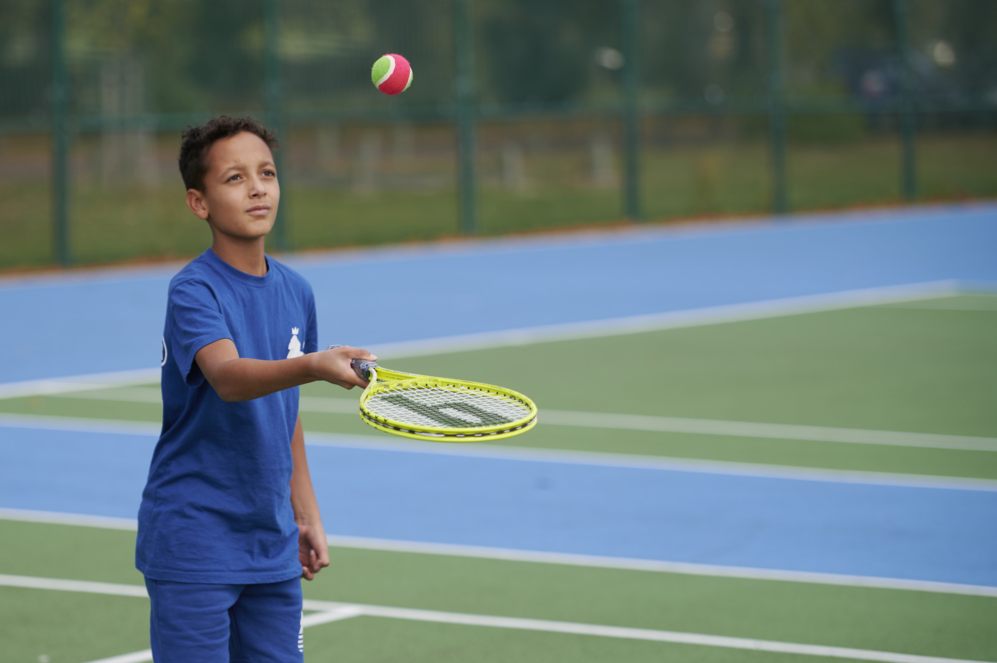 Young boy with tennis racket and tennis ball on tennis court in Moor Park
