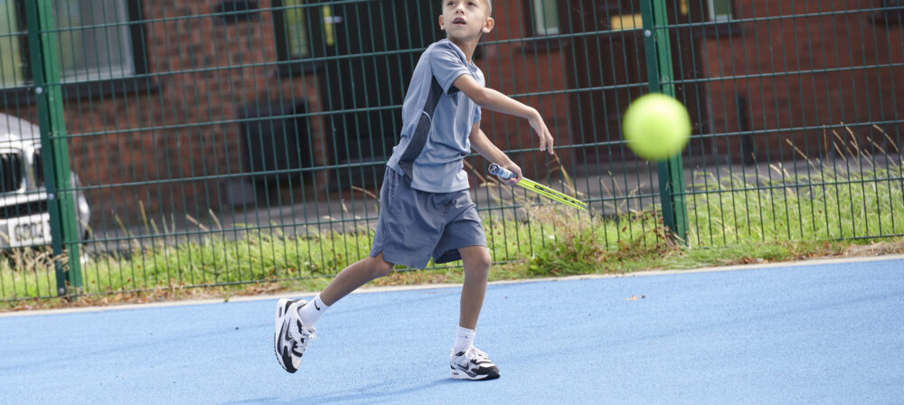 Young boy with tennis racket and ball playing tennis in Moor Park