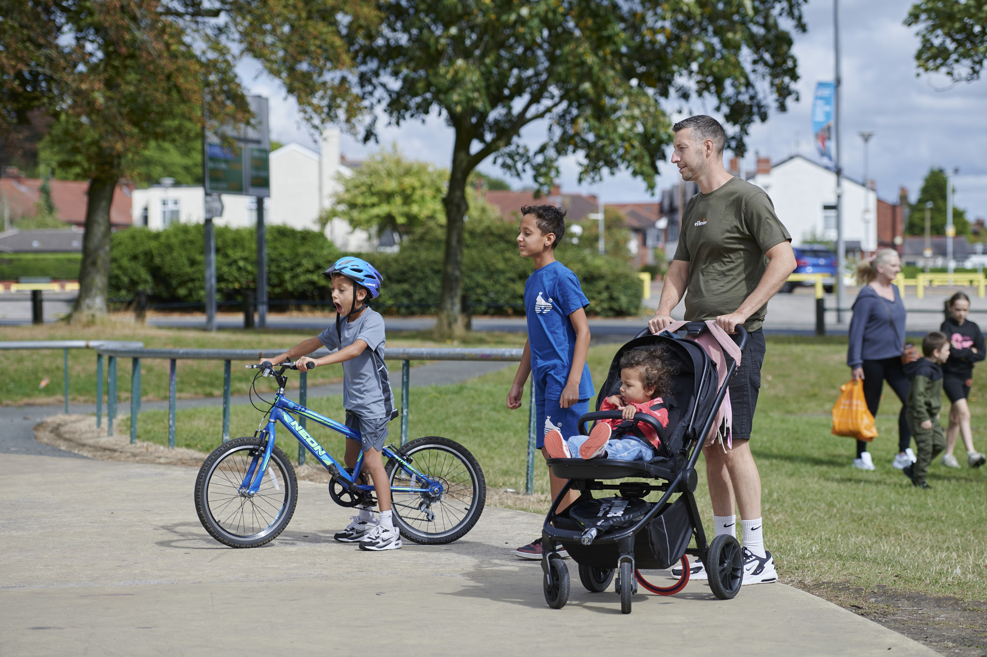 Male pushing pram with young girl, one boy scottering and one boy walking